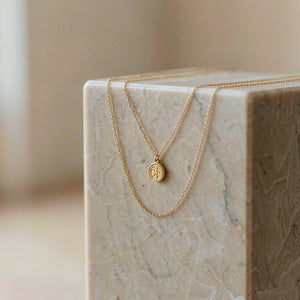Gold coin pendant necklace over a marble block — Offat